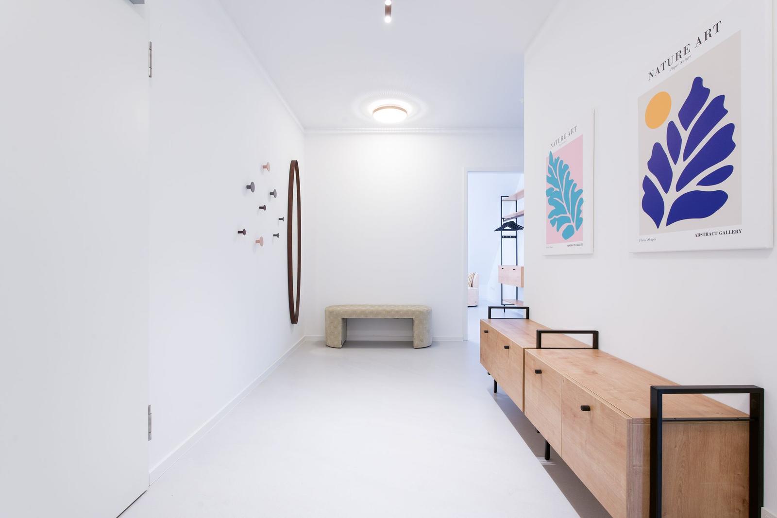 Hallenflur mit Holzschrank, Wandkunst und Sitzbank. Weiße Wände und Boden.