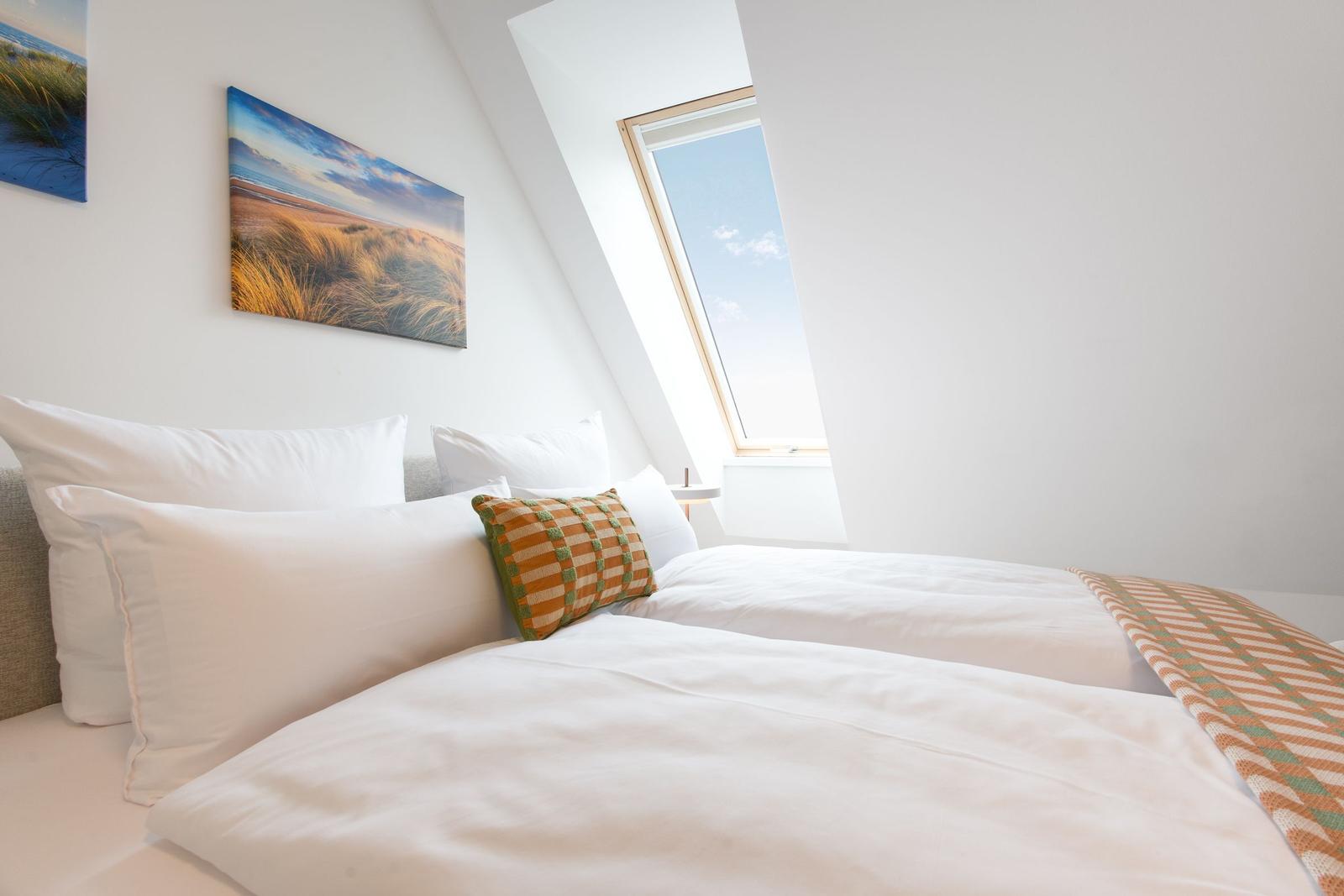 Schlafzimmer mit Dachfenster, Bett mit Kissen und Wandbildern.