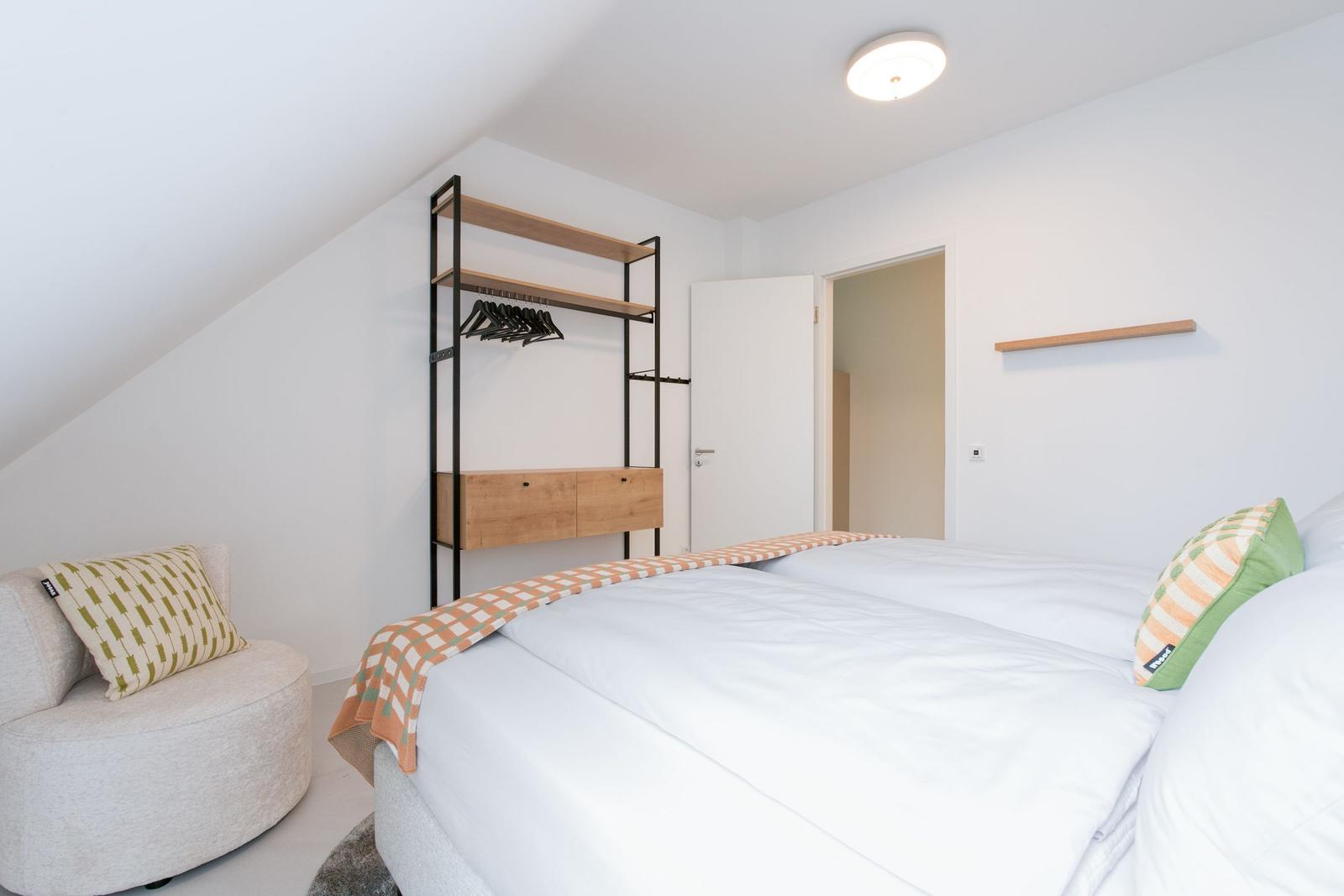 Schlafzimmer mit Doppelbett, Kleiderschrank und Sitzgelegenheit unter Dachschrägen.