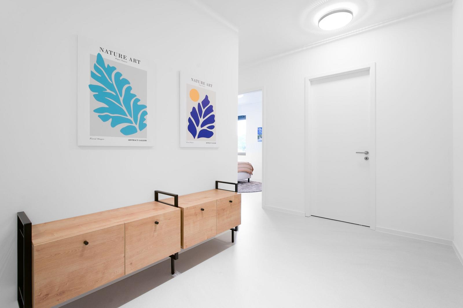 Flur mit Holzschrank und zwei Wandbildern. Tür und Blick in das Schlafzimmer.