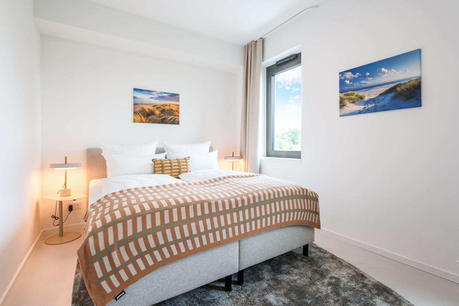 Schlafzimmer mit Bett, Wandbildern und Fenster.