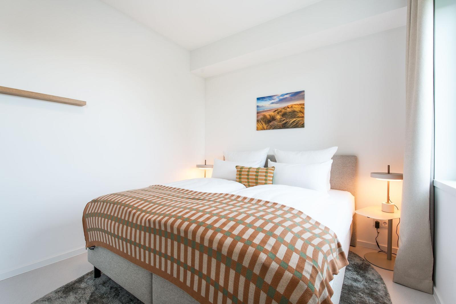 Schlafzimmer mit Bett, Wandbild und Nachttischlampen.