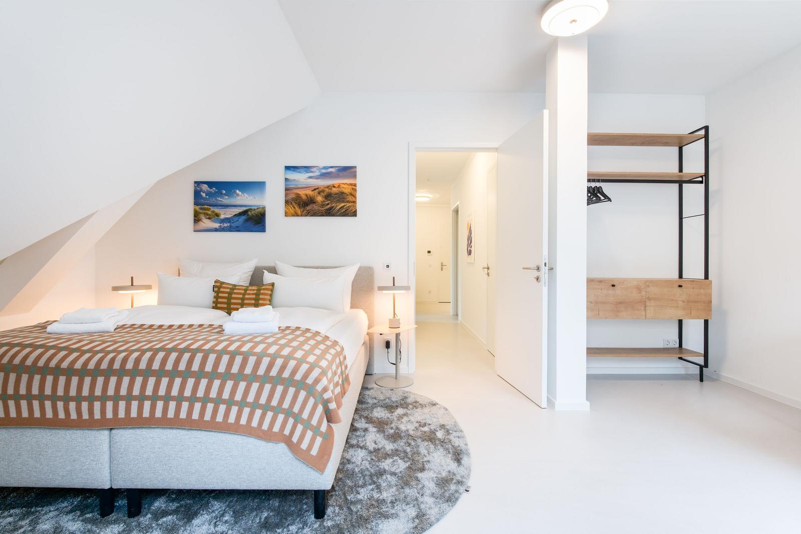 Schlafzimmer mit Dachschräge, Bett, Wandbildern und Kleiderschrank.