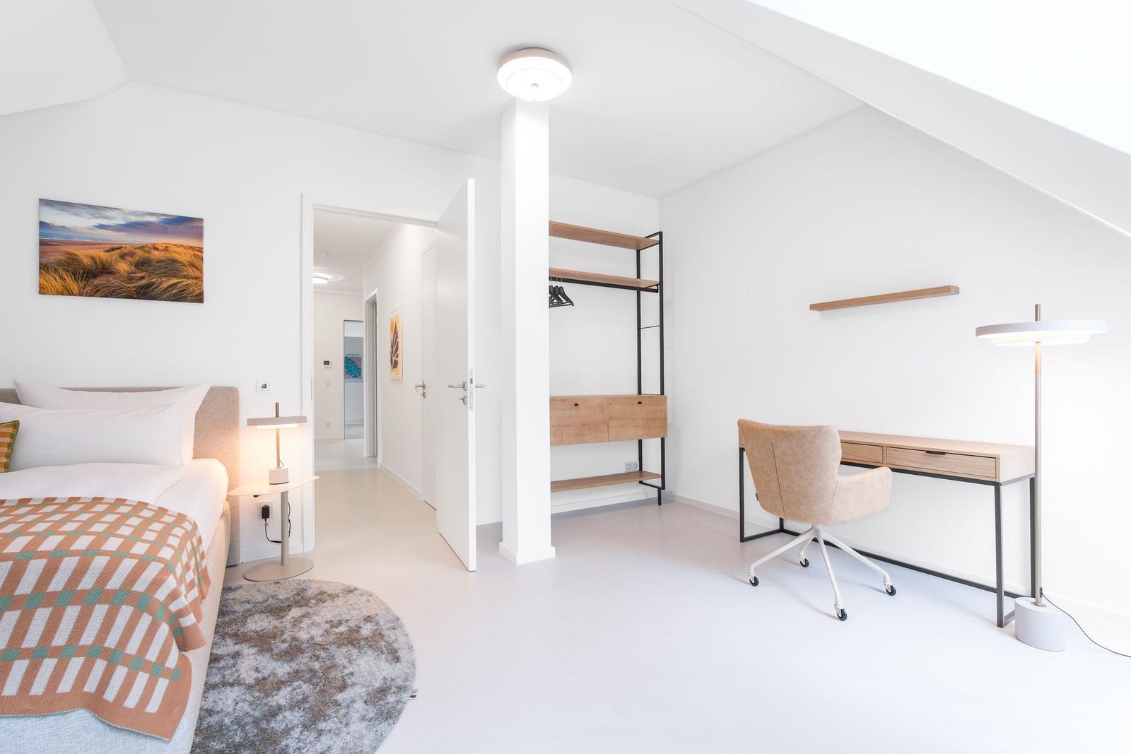Schlafzimmer mit Bett, Schreibtisch und Kleiderschrank. Wandbild und Stehlampe sichtbar.