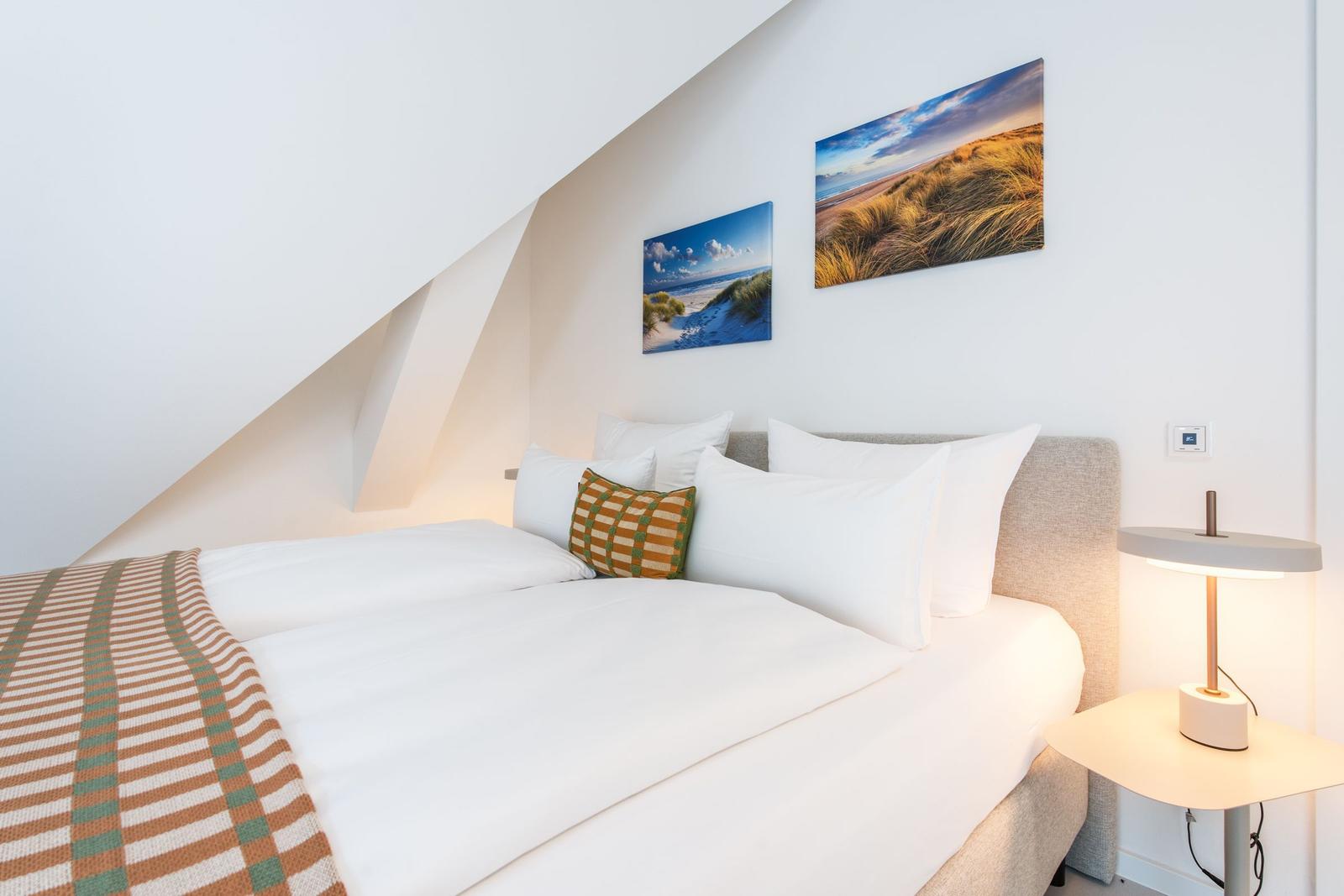 Schlafzimmer mit Bett, Kissen und Wandbildern an schräger Wand.