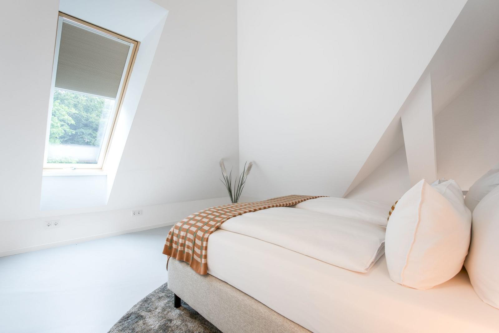 Schlafzimmer mit Dachschräge, Bett und Dachfenster mit Blick auf Grün.