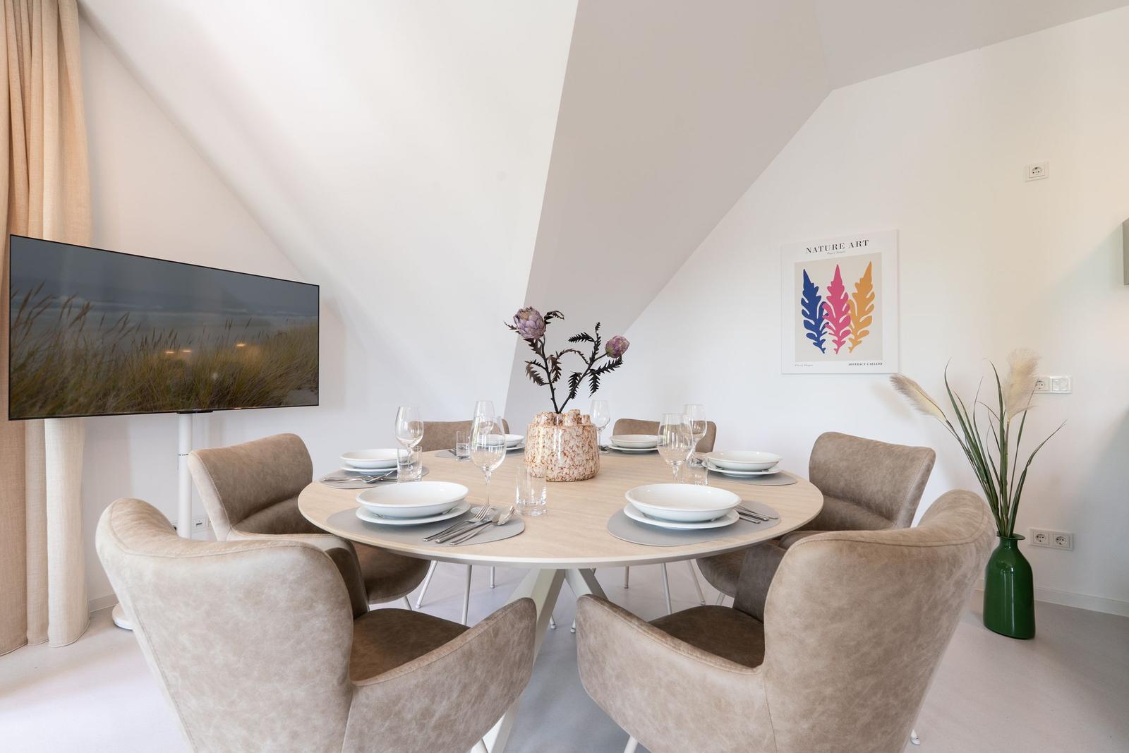 Rundes Esszimmer mit sechs Stühlen, Tischdekoration und Wandbild.