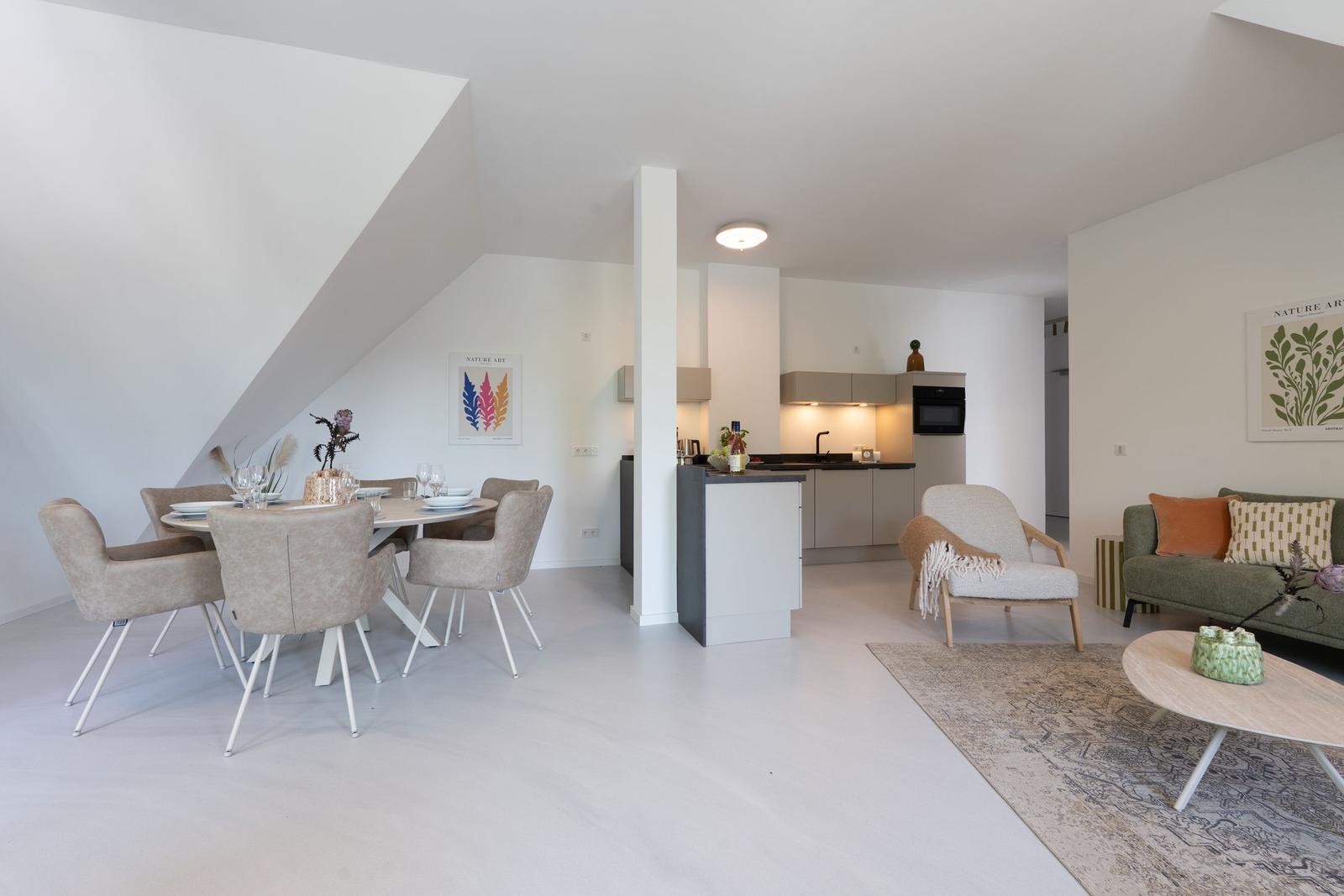 Wohn- und Essbereich mit Küche unter Dachschrägen. Moderne Einrichtung mit Sofa, Stühlen und Tisch.