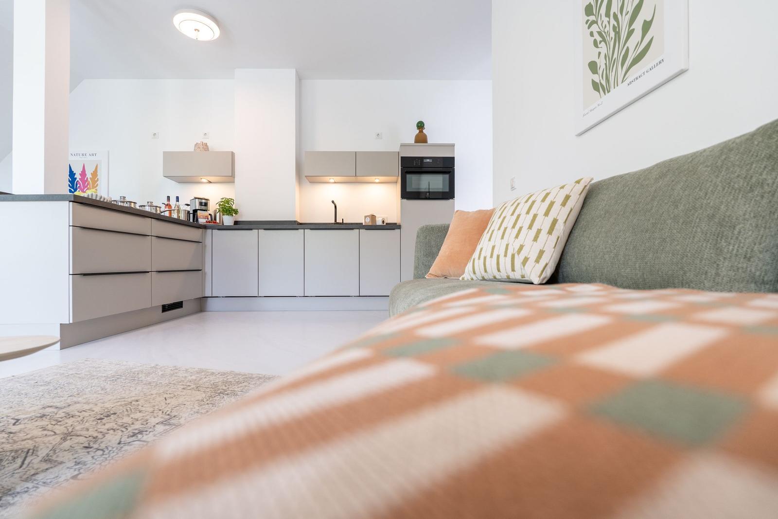 Ein Wohnbereich mit Sofa, Küchenzeile und Wandbild.