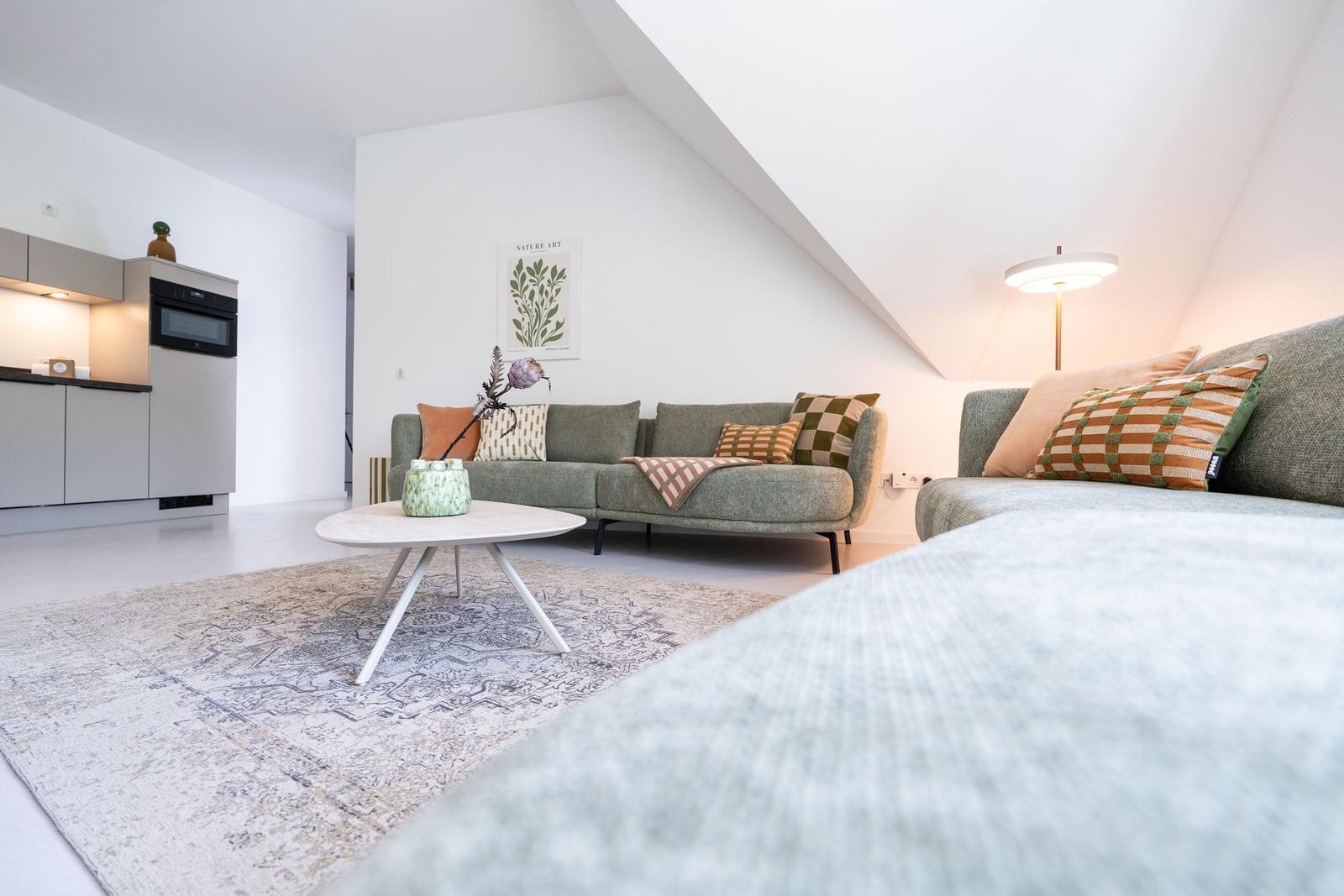 Wohnbereich mit Sofa, Couchtisch und Küchenzeile unter Dachschräge.