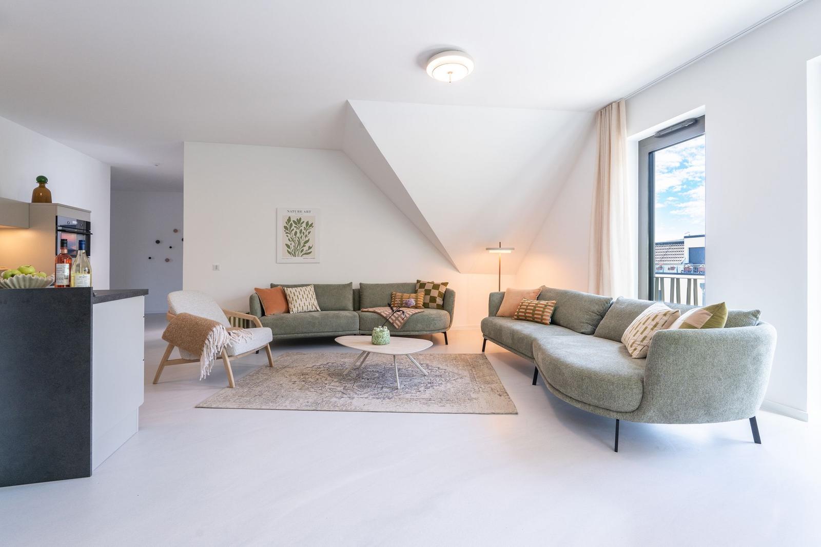 Wohnbereich mit zwei grauen Sofas, runden Tisch und Balkonansicht.