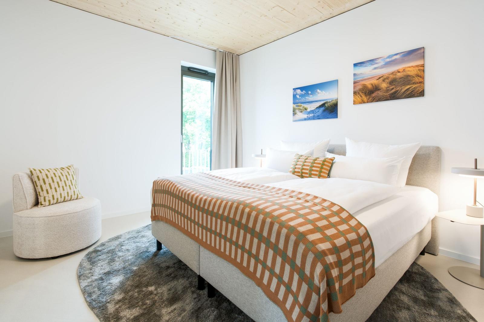 Schlafzimmer mit Doppelbett, Sessel und Fenster zur Terrasse.