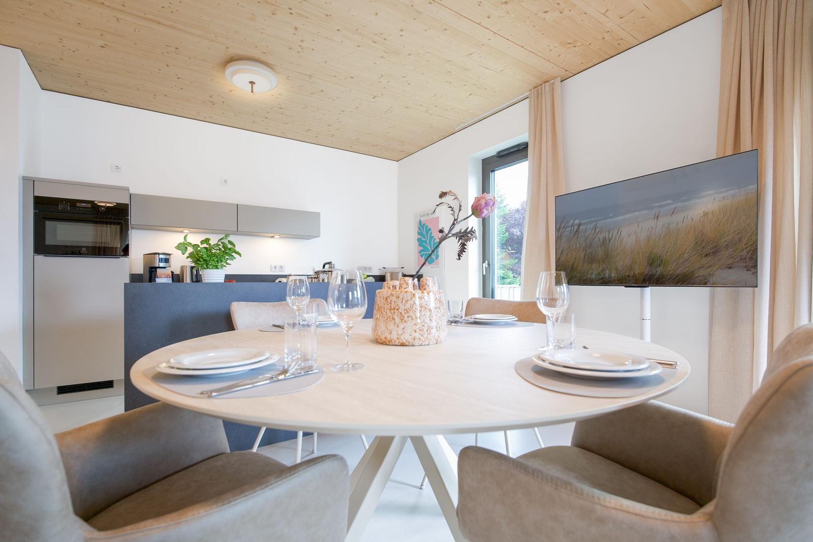Runder Esstisch mit Stühlen, Küchenzeile und Fernseher an der Wand.
