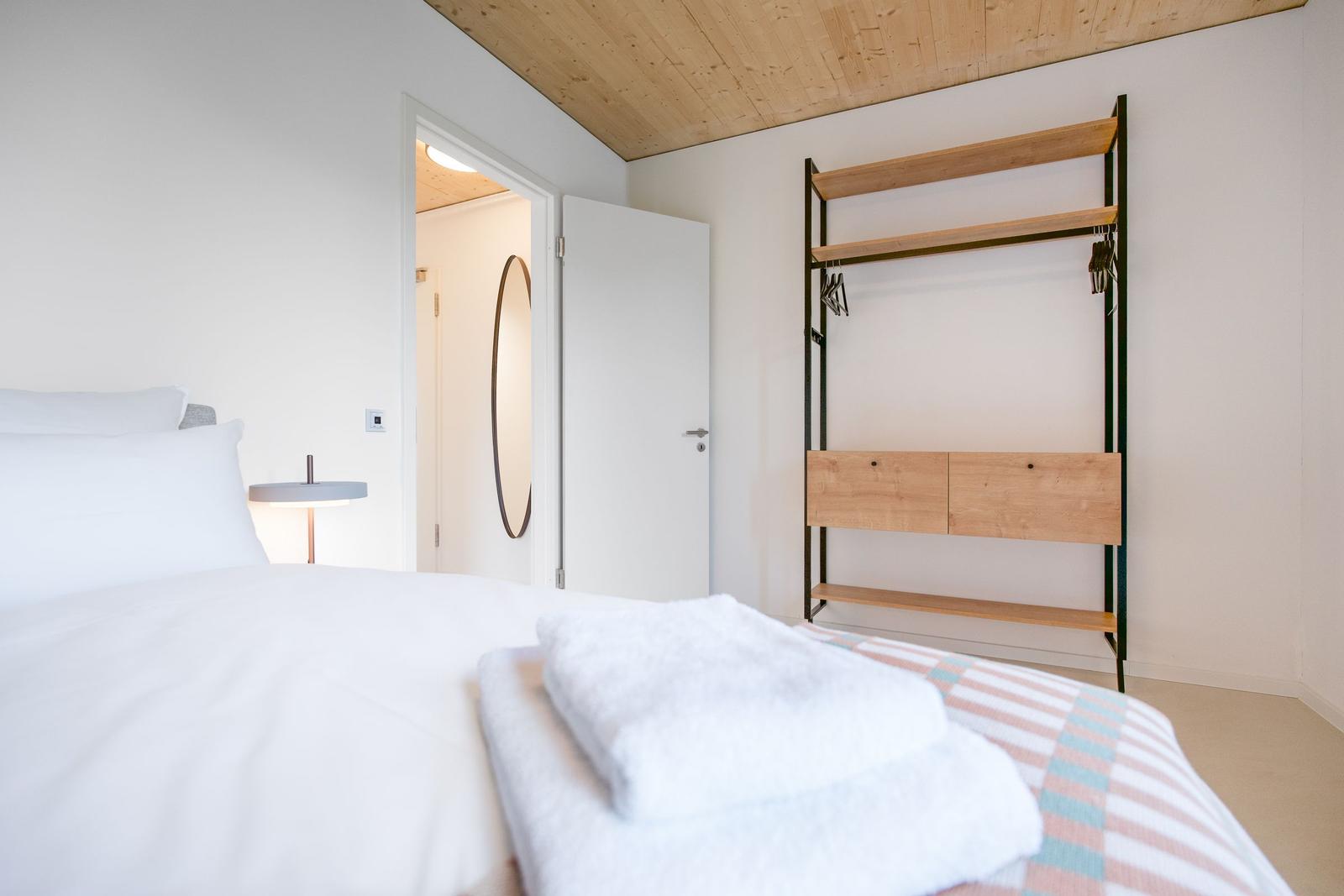 Schlafzimmer mit Bett, Kleiderständer und Tür zum Badezimmer.