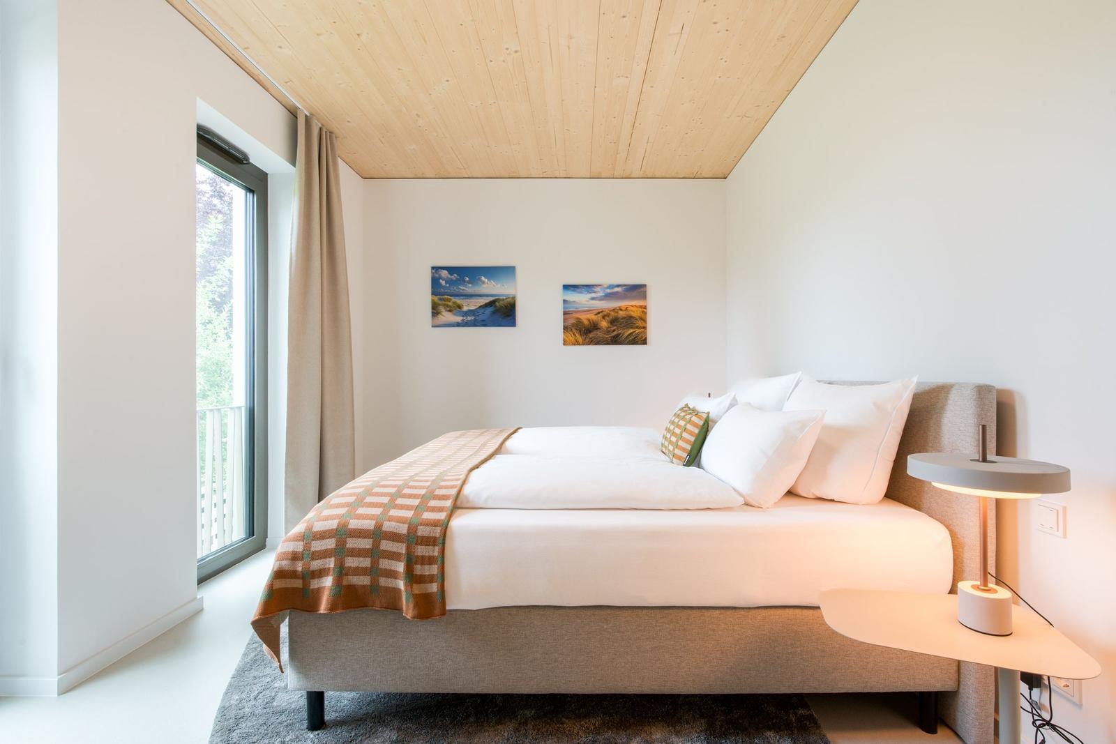Schlafzimmer mit Bett, Fenster und Wandbildern.