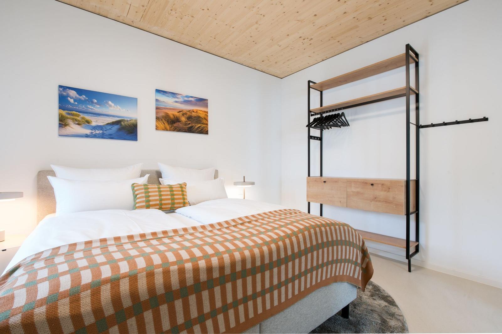 Schlafzimmer mit Bett, Kleiderständer und Wandbildern.