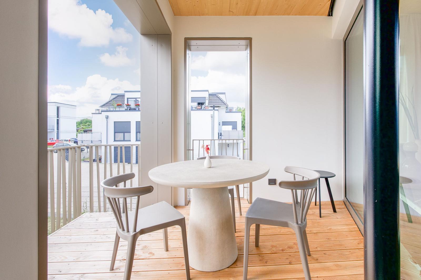 Terrasse mit runden Tisch und Stühlen, Holzboden und Blick auf Wohngebäude.