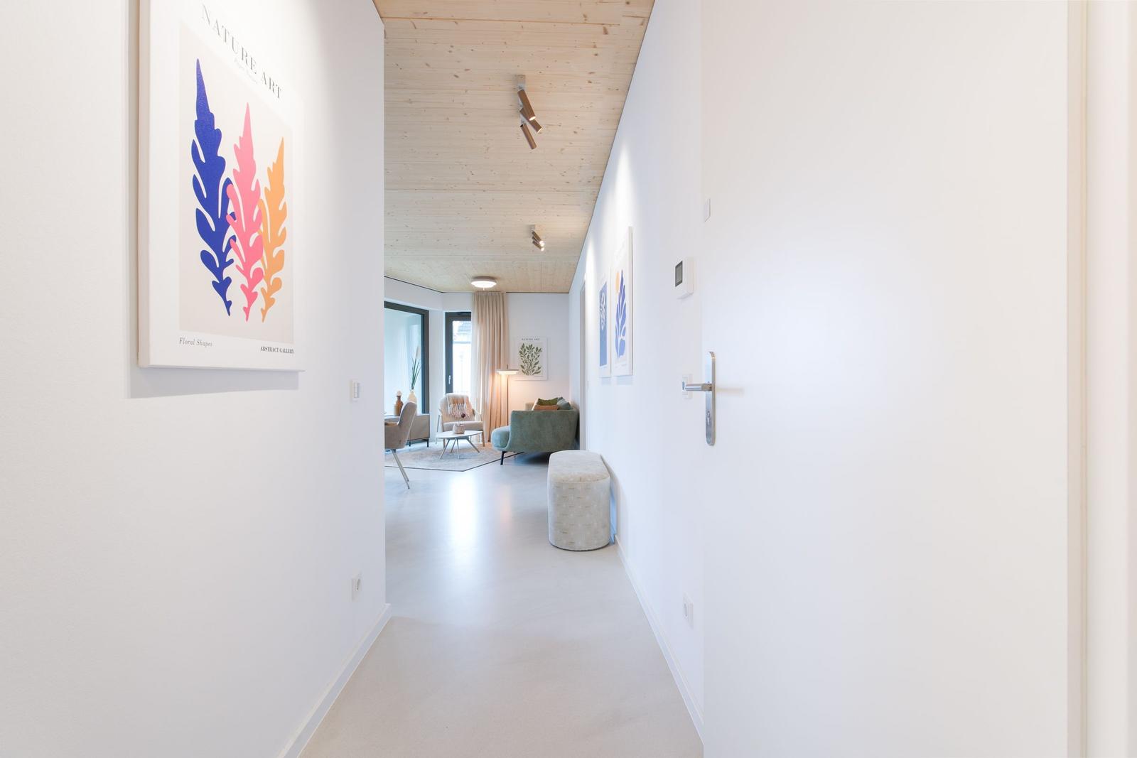 Flur mit weißen Wänden, Holzdecke und Kunstwerk an der Wand. Blick in das Wohnzimmer.