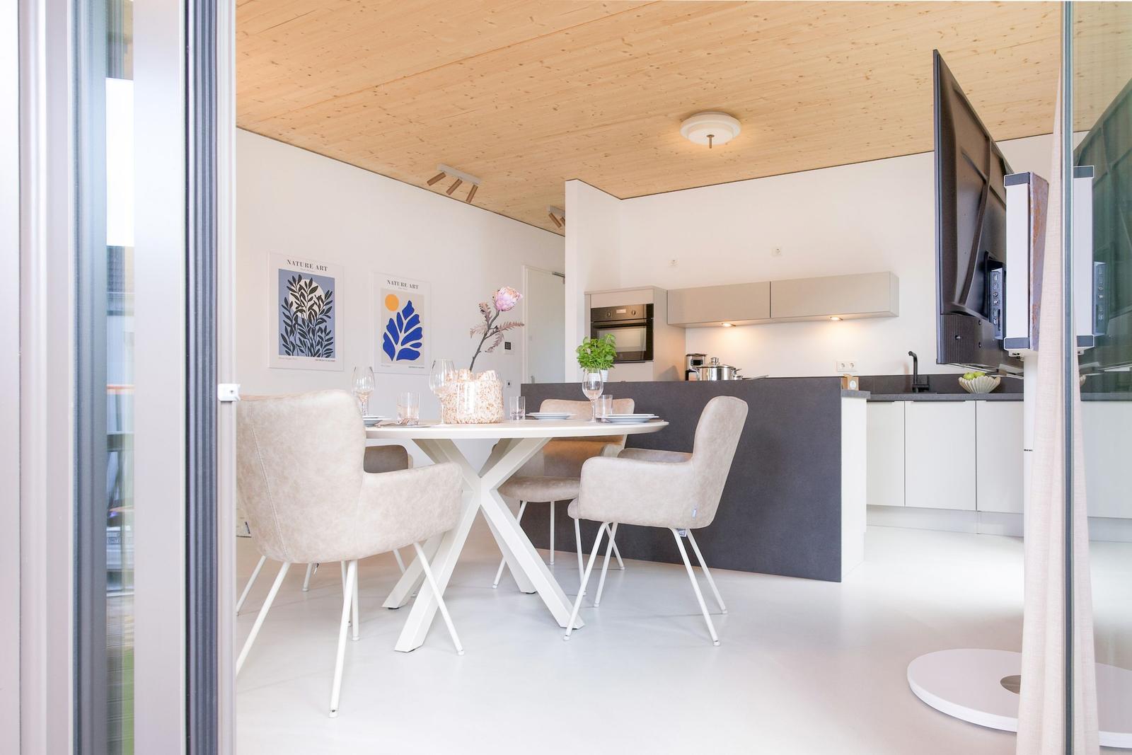 Essbereich mit Tisch und Stühlen, Kücheninsel und TV. Holzdecke und weiße Wände.