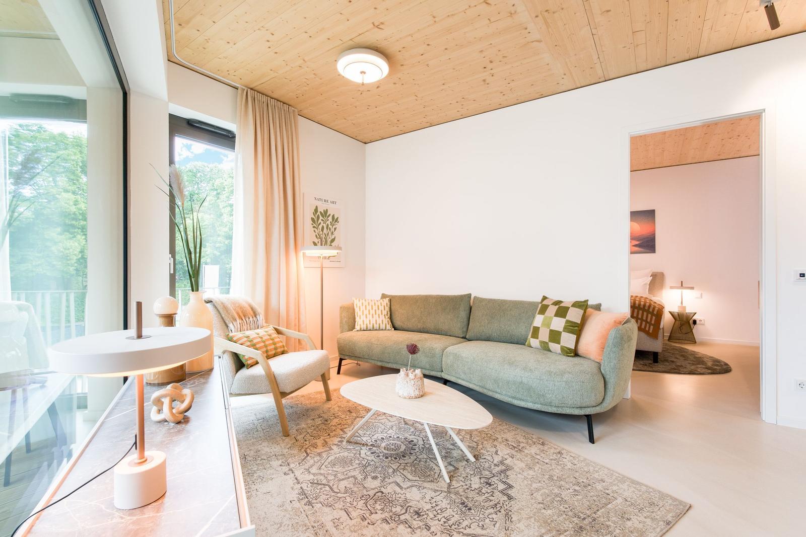 Wohnzimmer mit Sofa, Sessel und Tisch. Holzdecke und große Fenster.