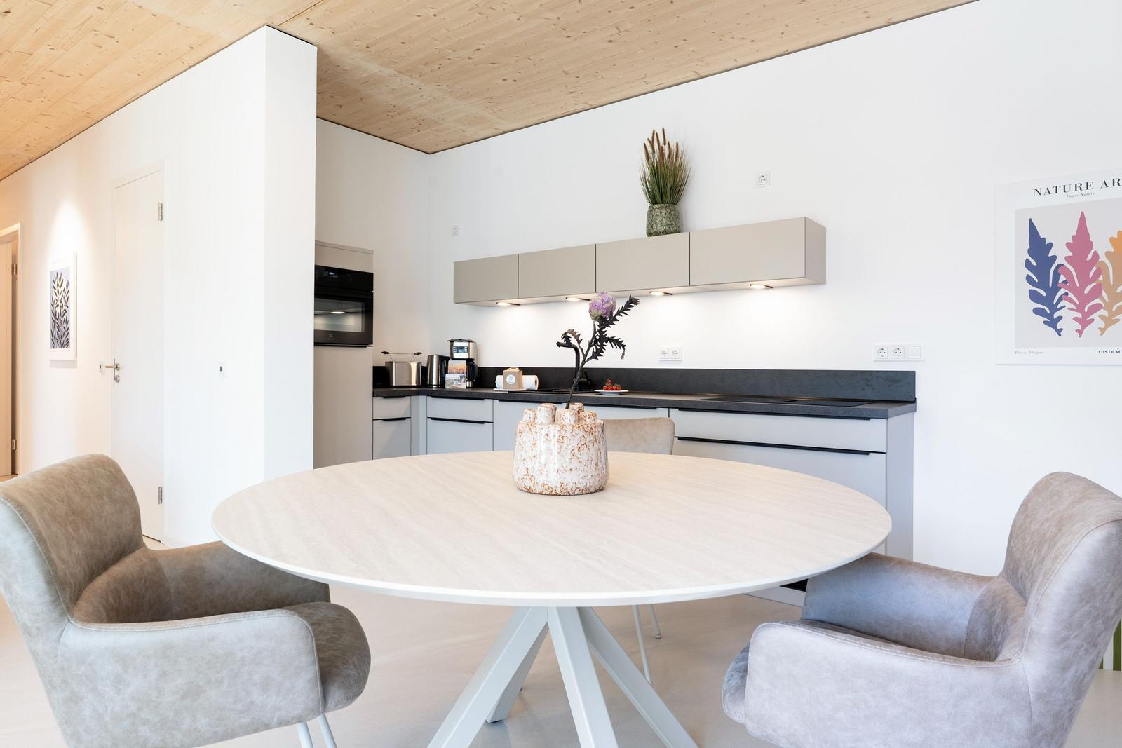 Rundtisch mit Stühlen vor moderner Küche mit Holzdecke und Wandbild.