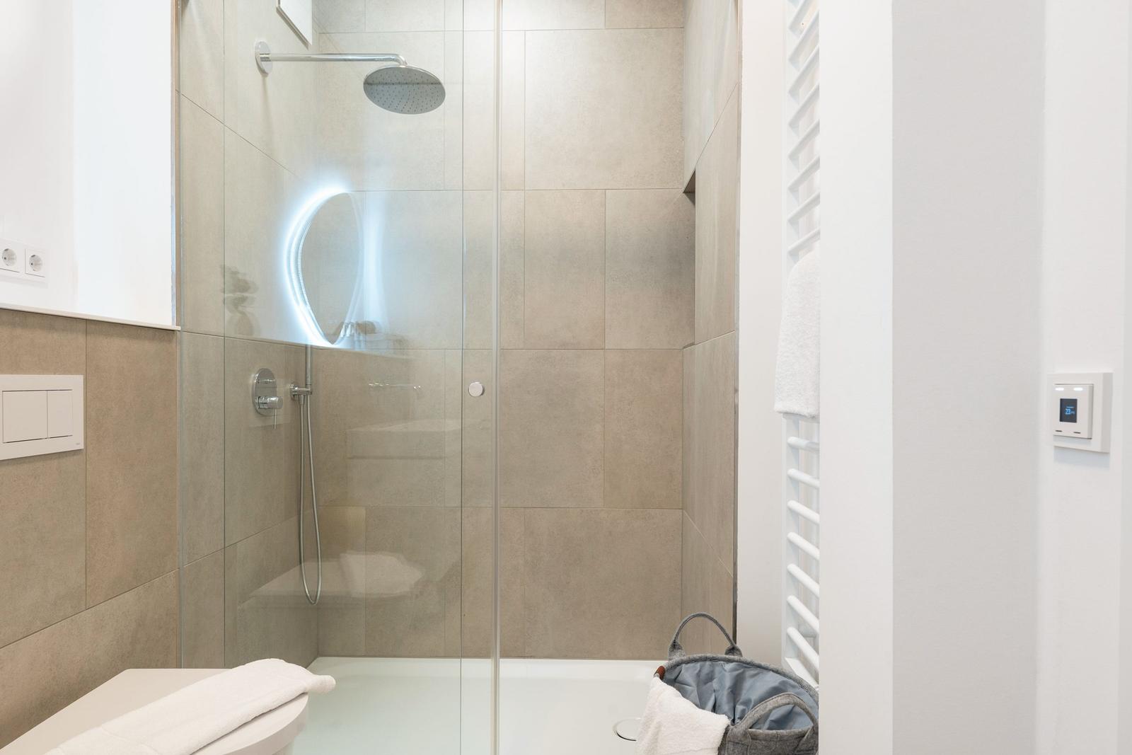 Dusche mit Glaswand, beleuchtetem Spiegel und Handbrause.