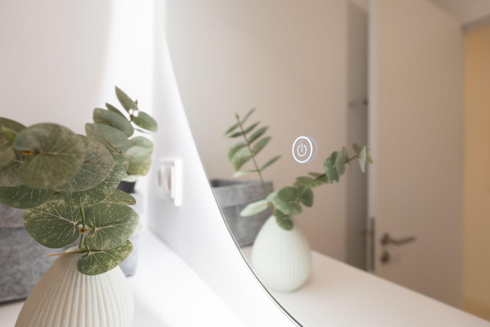 Spiegel mit Touch-Steuerung und Pflanze in Vase auf weißem Tisch