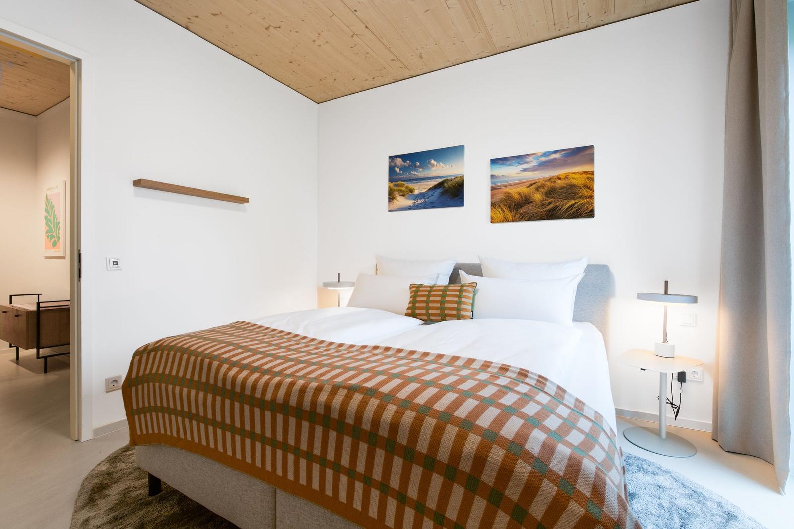 Schlafzimmer mit Bett, Wandbildern und Holzdecke.