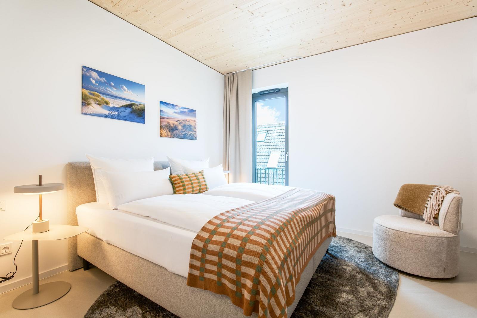 Doppelbett mit Kissen und Decke, Sessel, Lampe und Wandbilder
