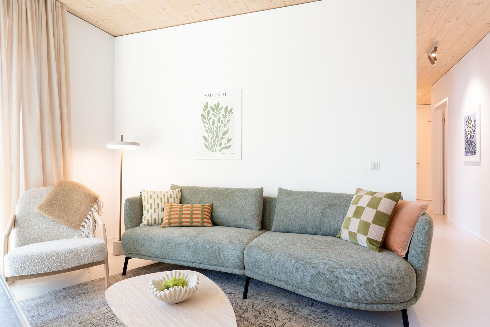 Ein Wohnzimmer mit einem grauen Sofa, einem weißen Sessel und einer runden Tischplatte.