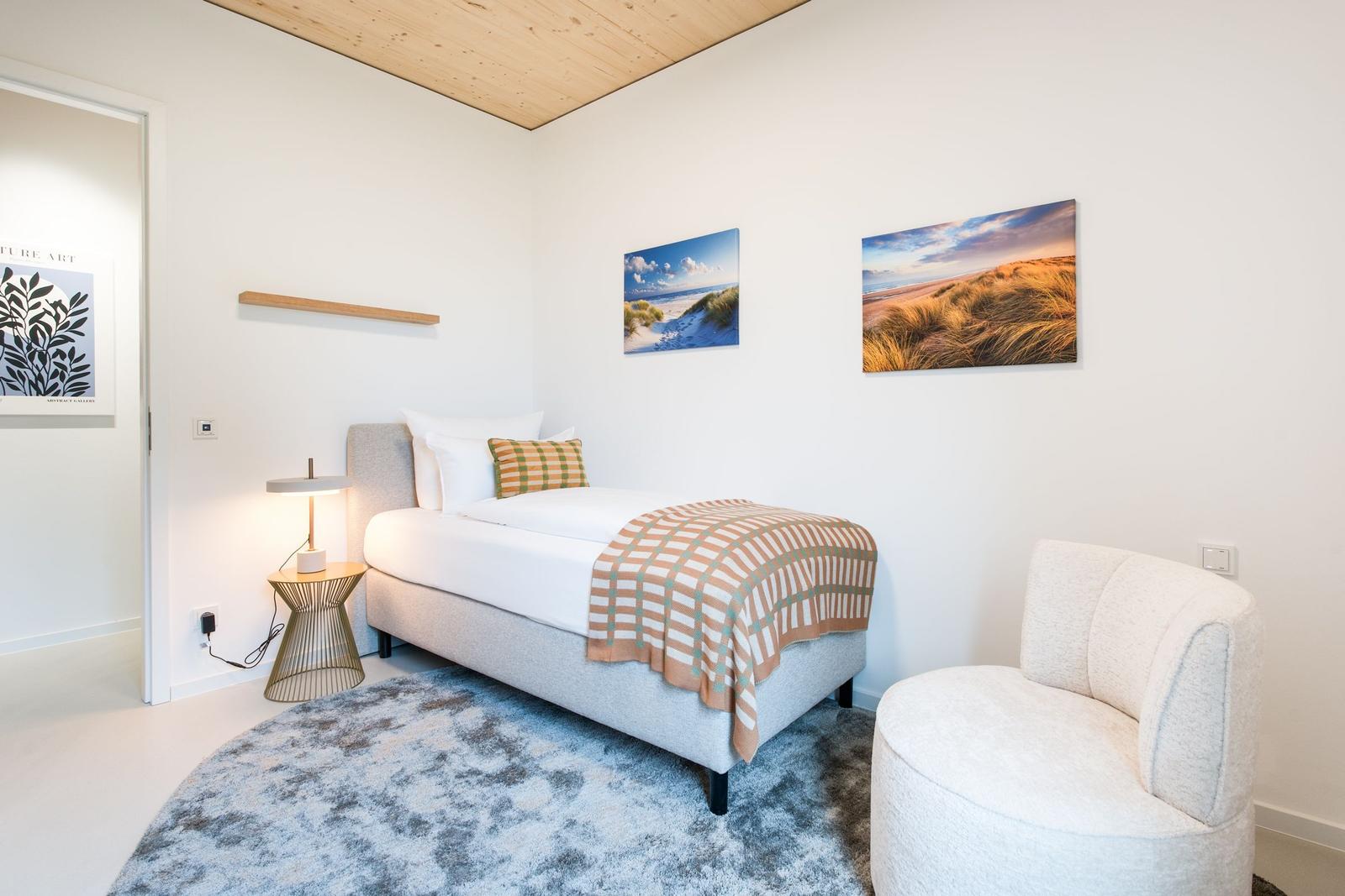 Schlafzimmer mit Bett, Sessel und Wandbildern.