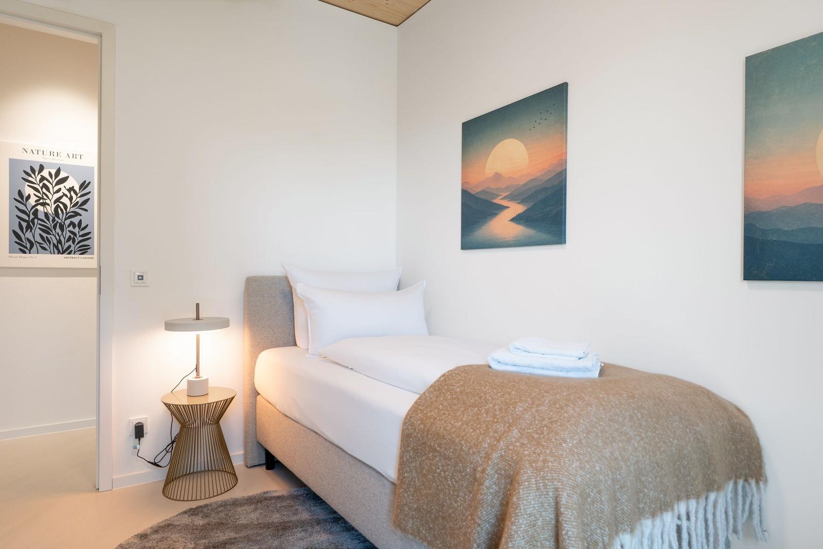 Ein Schlafzimmer mit Bett, Decke, Nachttisch und Wandbildern.