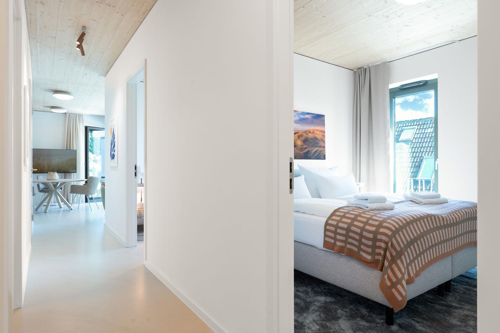 Schlafzimmer mit Bett, Fenster und Wandbild. Flur führt zum Essbereich.