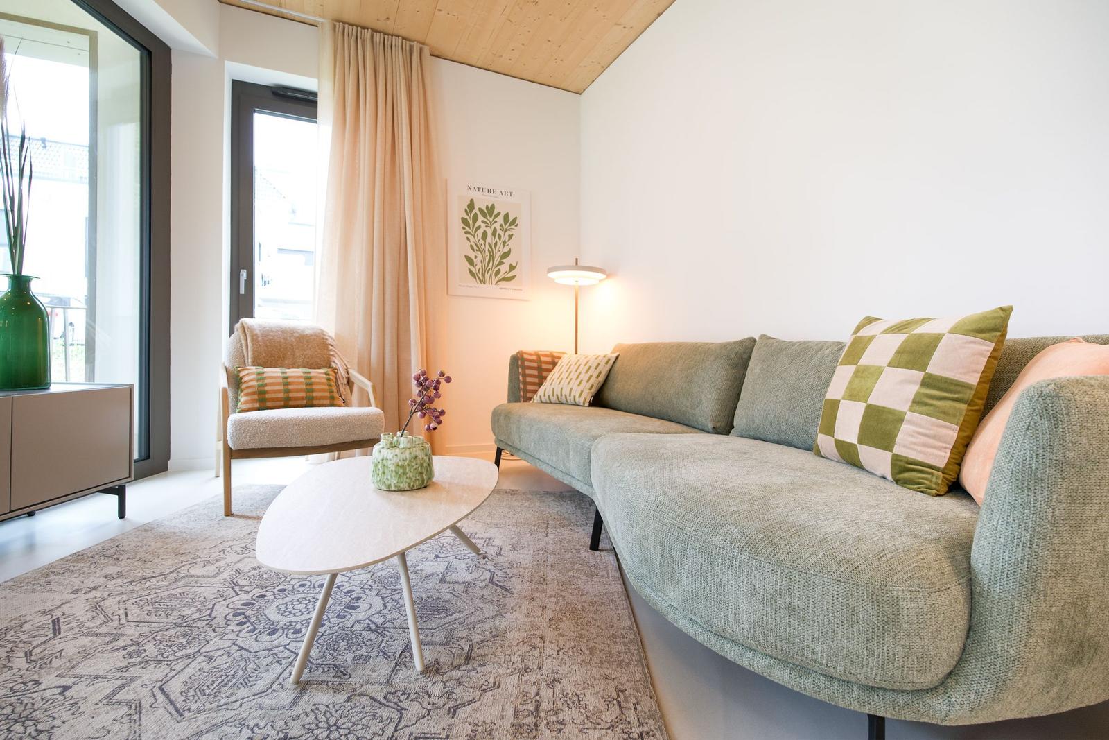 Ein Wohnzimmer mit Sofa, Sessel und Tisch. An der Wand hängt ein Bild.