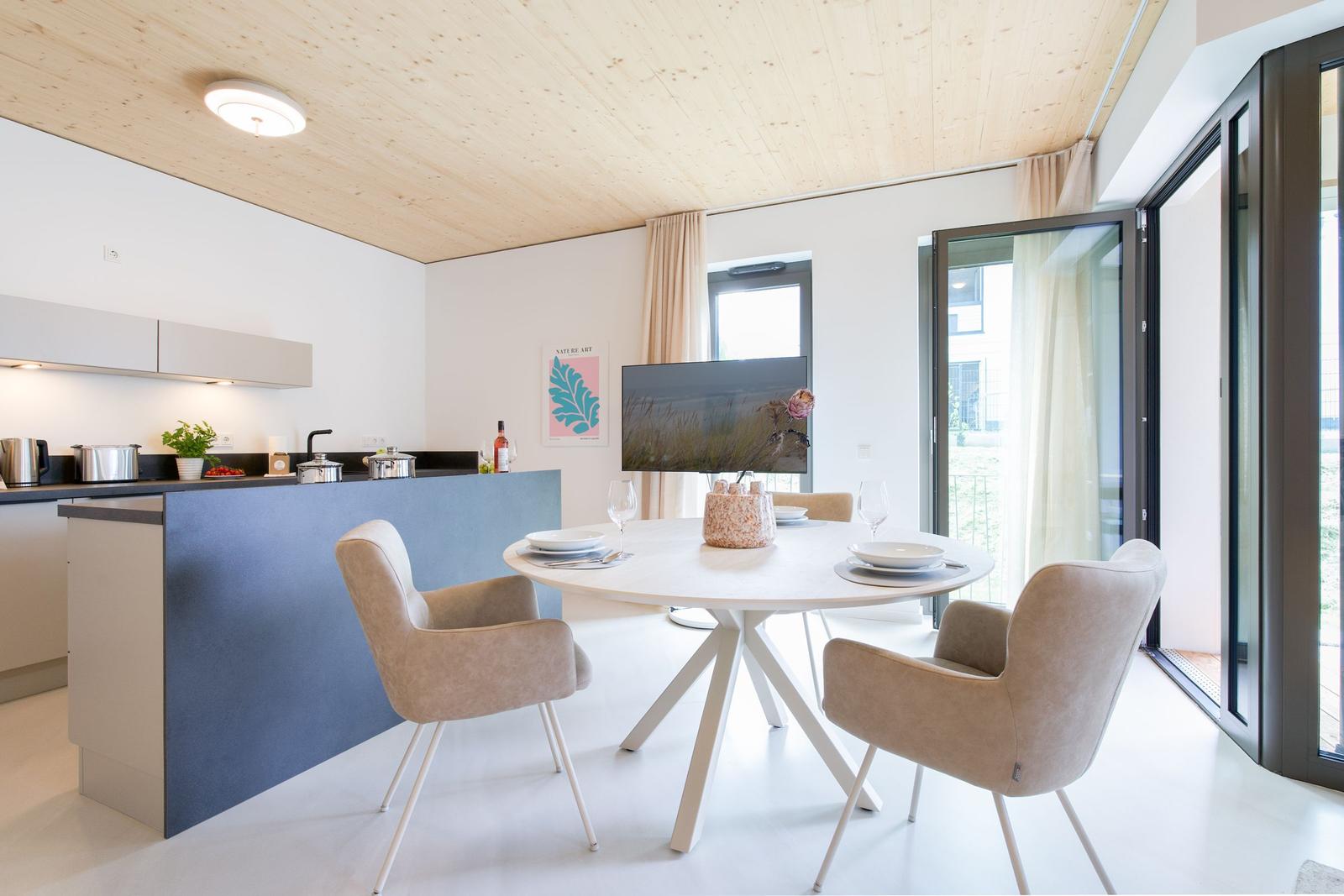 Küche und Essbereich mit runden Tisch, Stühlen und Glasfront zur Terrasse.
