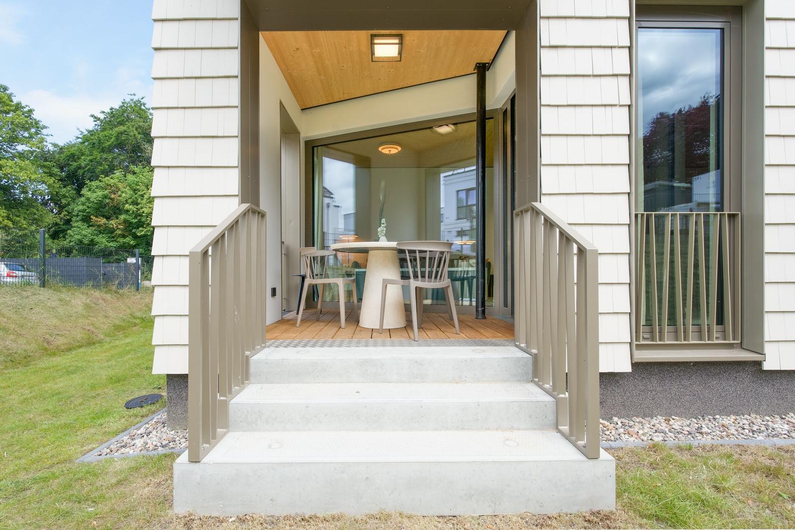 Haus mit Terrasse, Tisch und Stühlen. Holzdecke und Glaswände sichtbar.