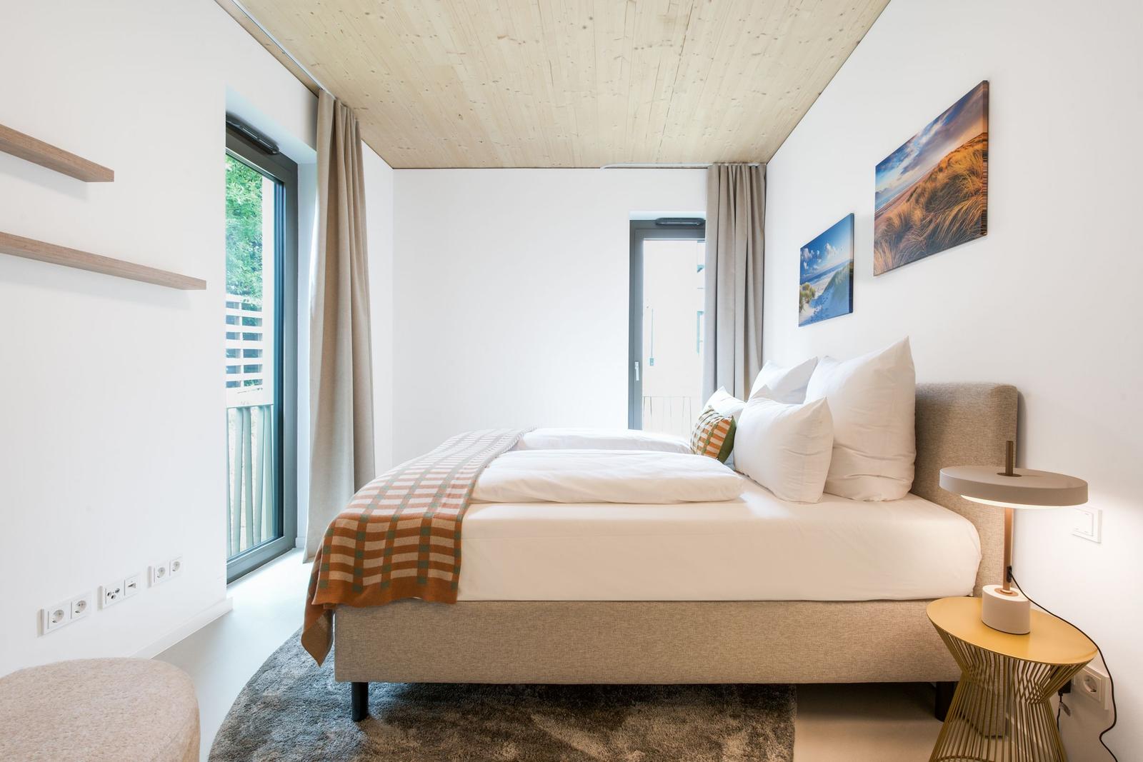 Schlafzimmer mit Bett, Wandbildern und Fenster zur Terrasse.