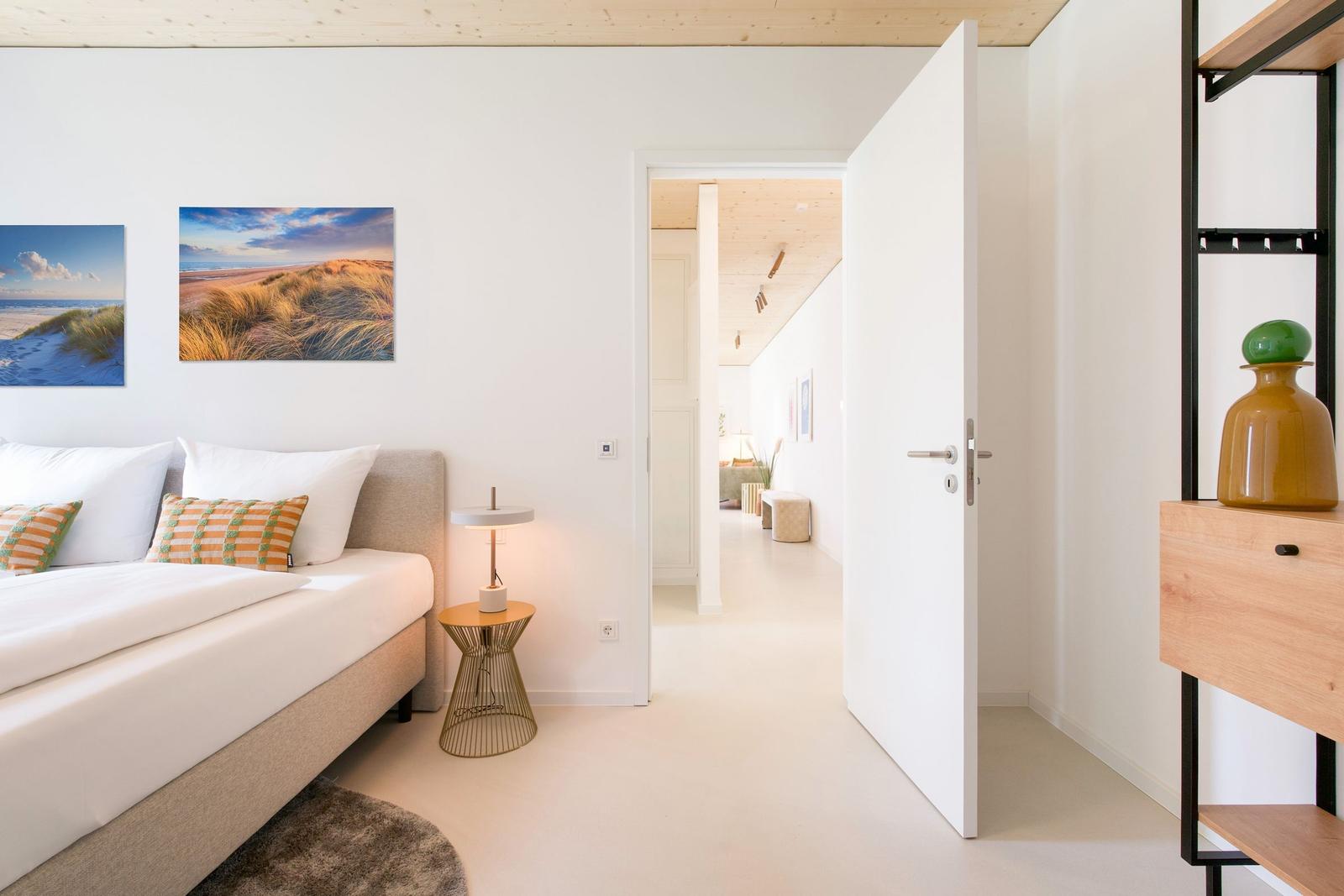 Schlafzimmer mit Bett, Nachttisch und Blick in Flur. Wandbild und Holzdecke sichtbar.