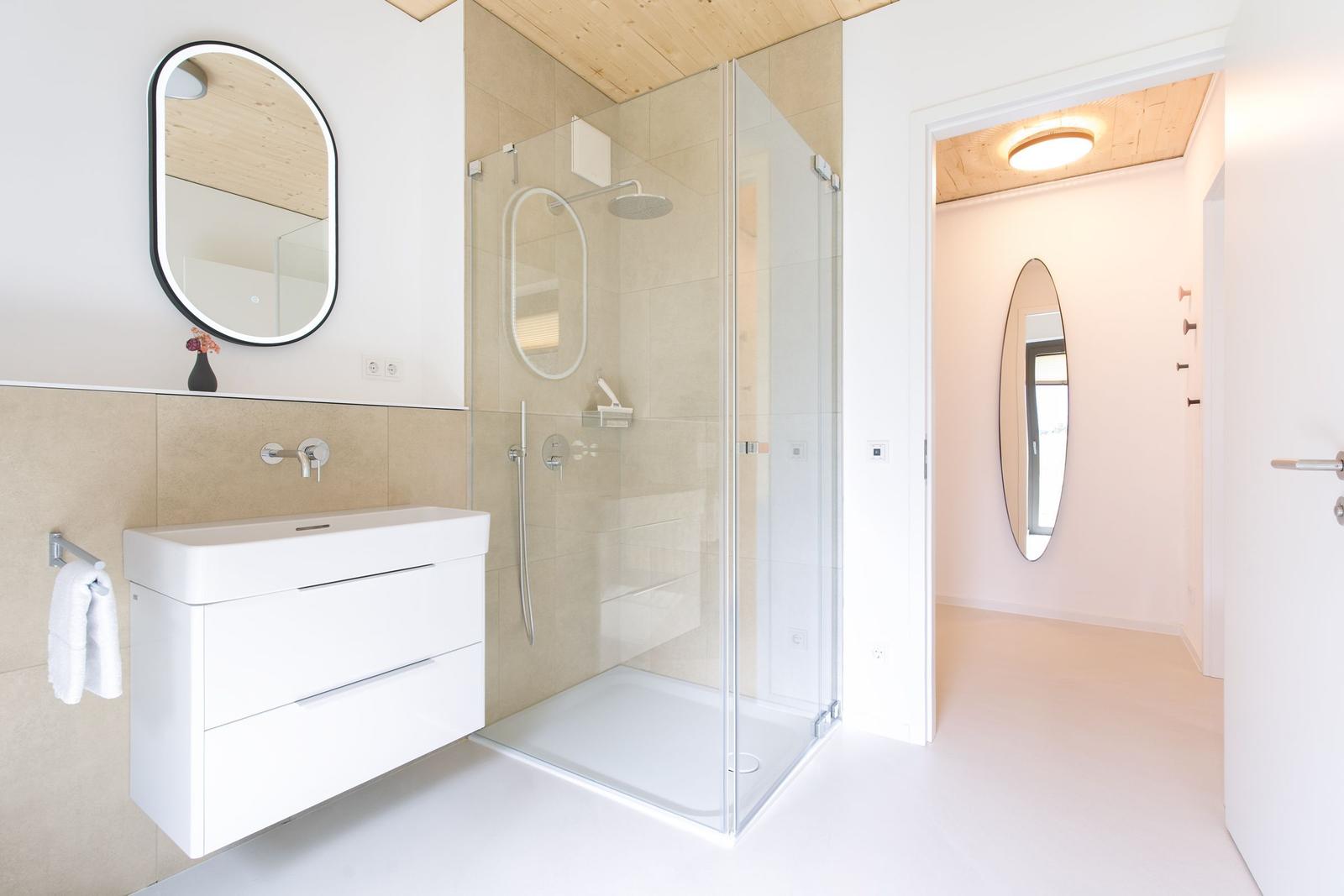 Badezimmer mit Dusche, Waschbecken und Spiegel. Holzdecke und helle Wände.
