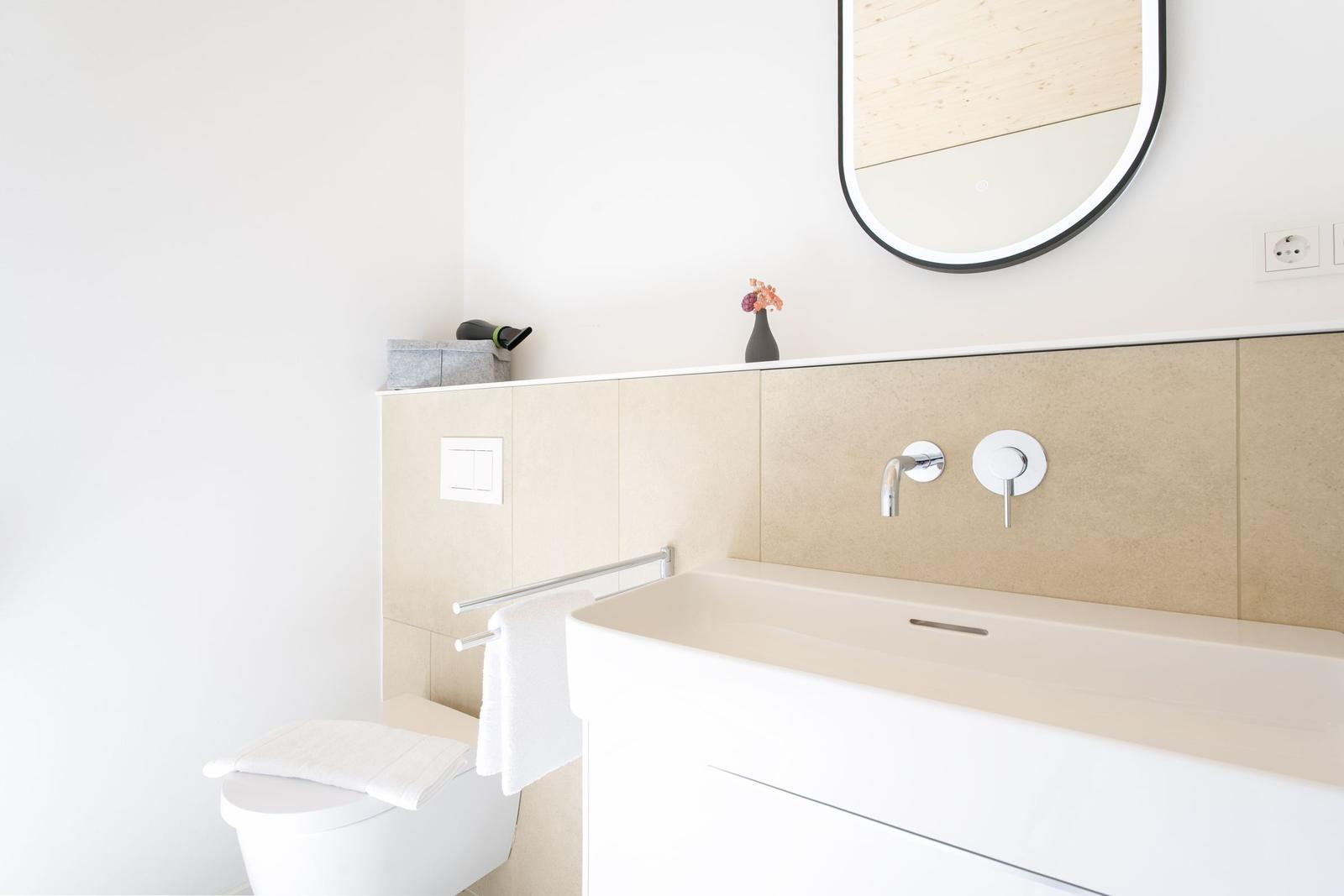 Badezimmer mit Waschbecken, Spiegel und Toilette. Helle Wände und moderne Armaturen.