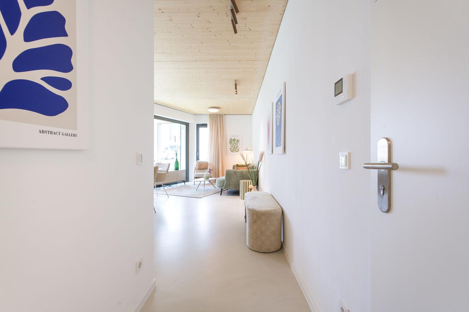 Flur mit Wandbild und Blick in Wohnbereich mit Sitzgelegenheiten und Holzdecke.