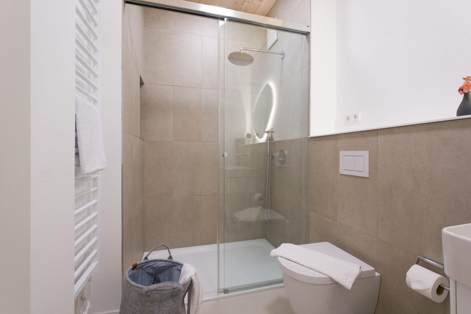 Badezimmer mit Dusche, Toilette und Waschbecken. Glaswand, Holzdecke und beige Fliesen.
