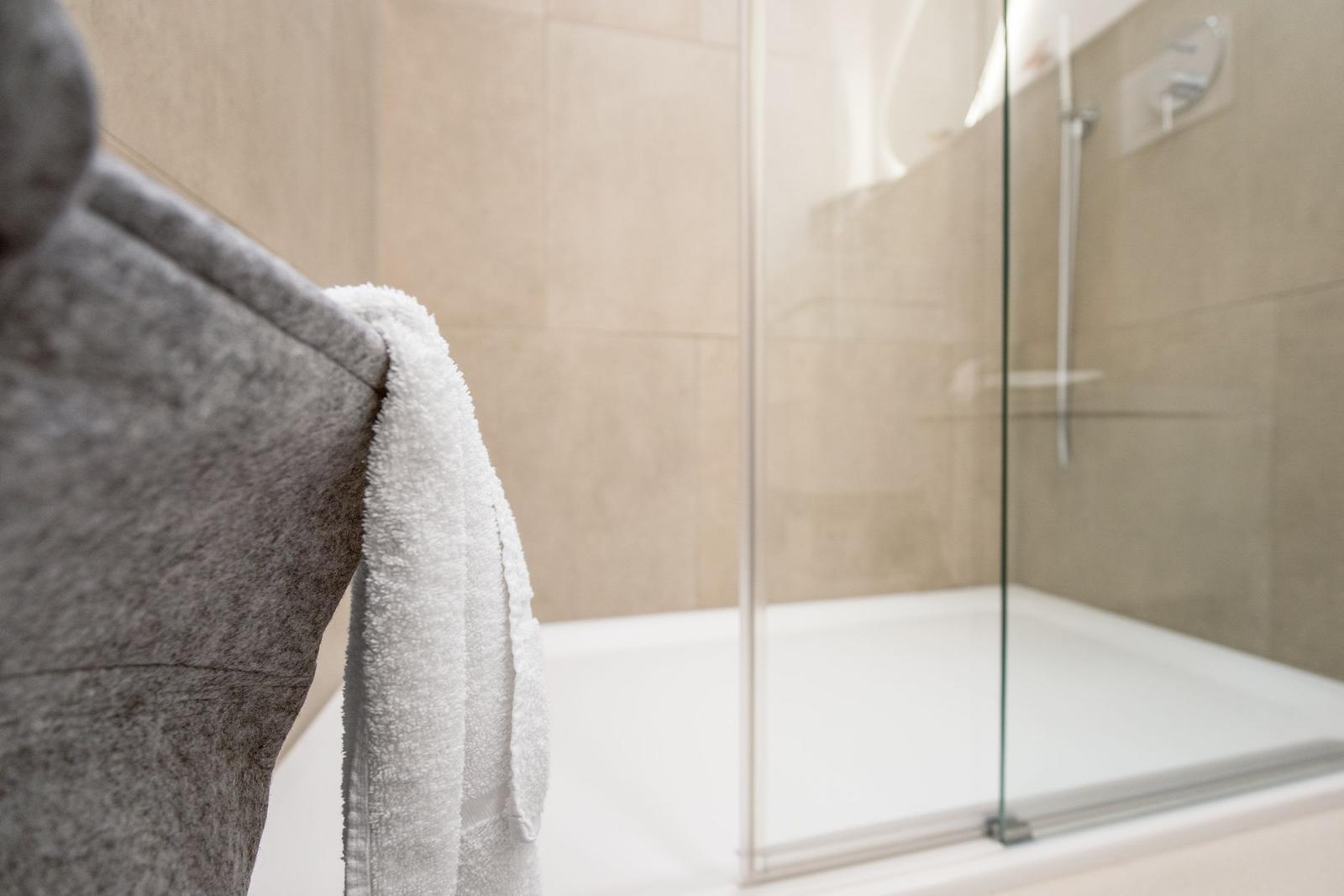 Dusche mit Glaswand und weiße Badewanne mit Handtuch.