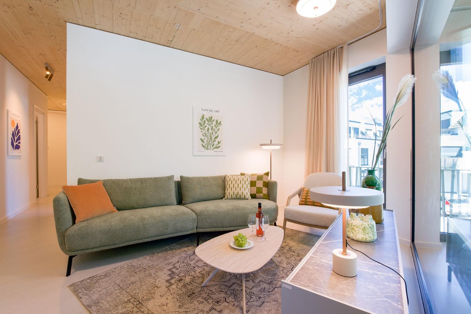 Wohnzimmer mit Sofa, Couchtisch und großem Fenster. Holzdecke und Wandbild sichtbar.