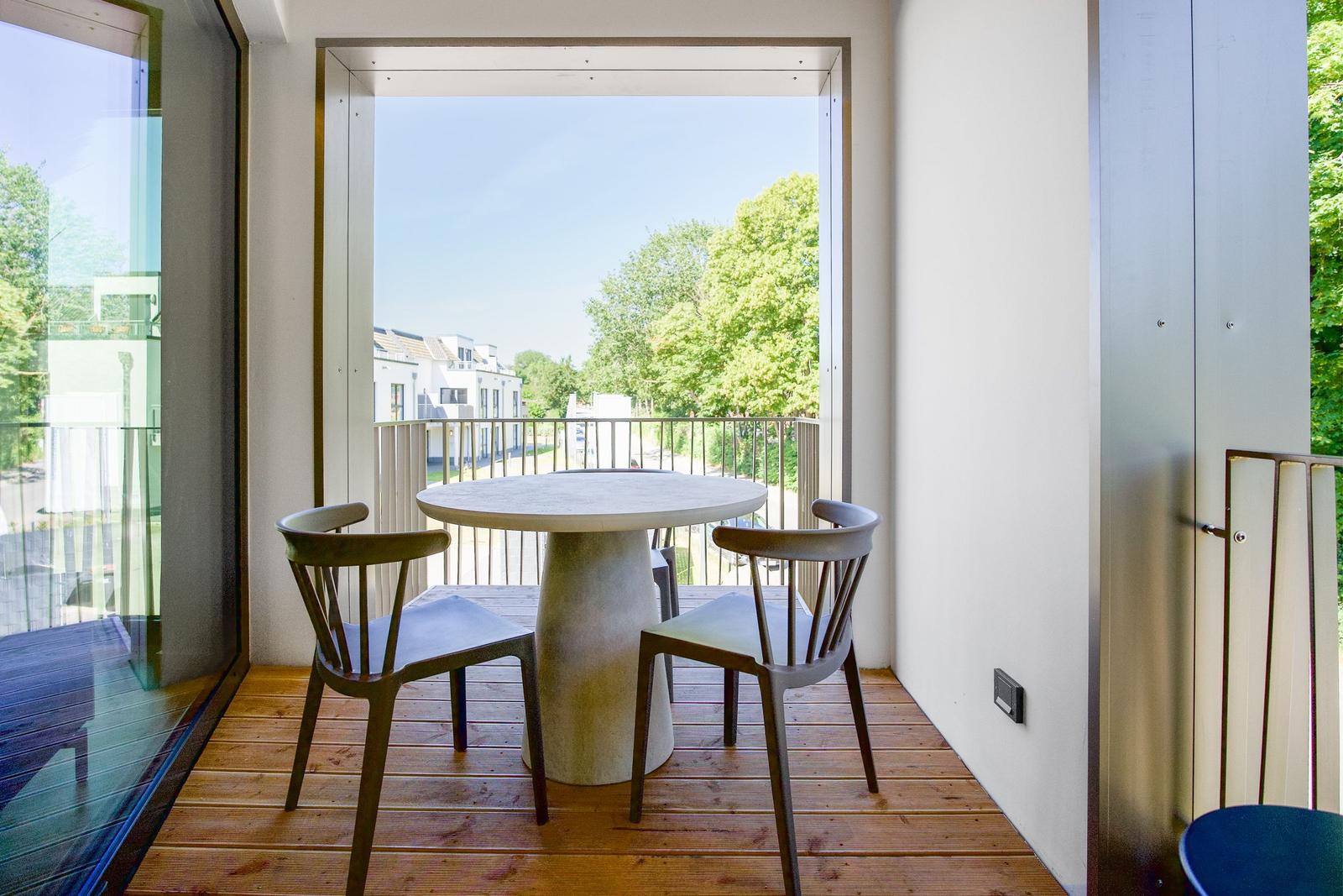 Terrasse mit runden Tisch und zwei Stühlen. Blick auf Grün und Gebäude.