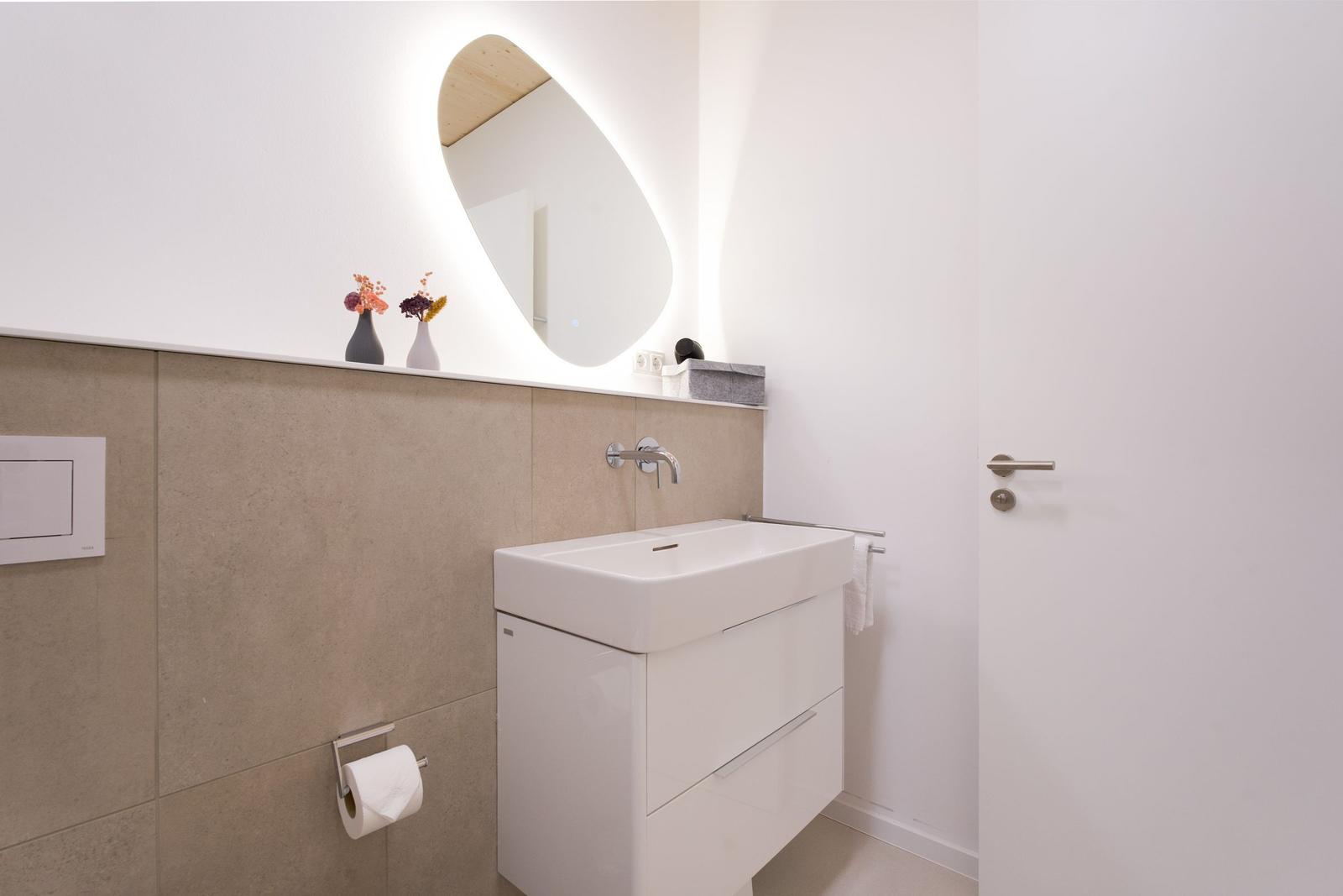 Badezimmer mit Waschbecken, Spiegel und Toilettenpapierhalter