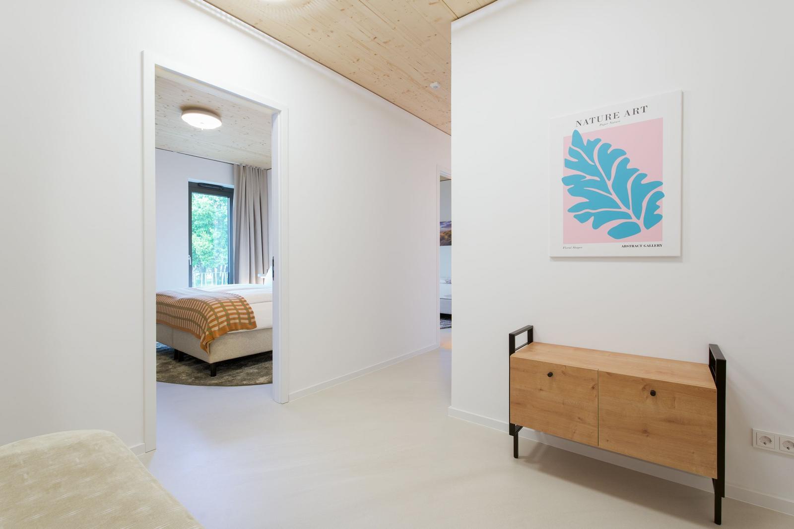 Flur mit Holzschrank und Wandbild. Durchgang zu Schlafzimmer mit Bett und Fenster.