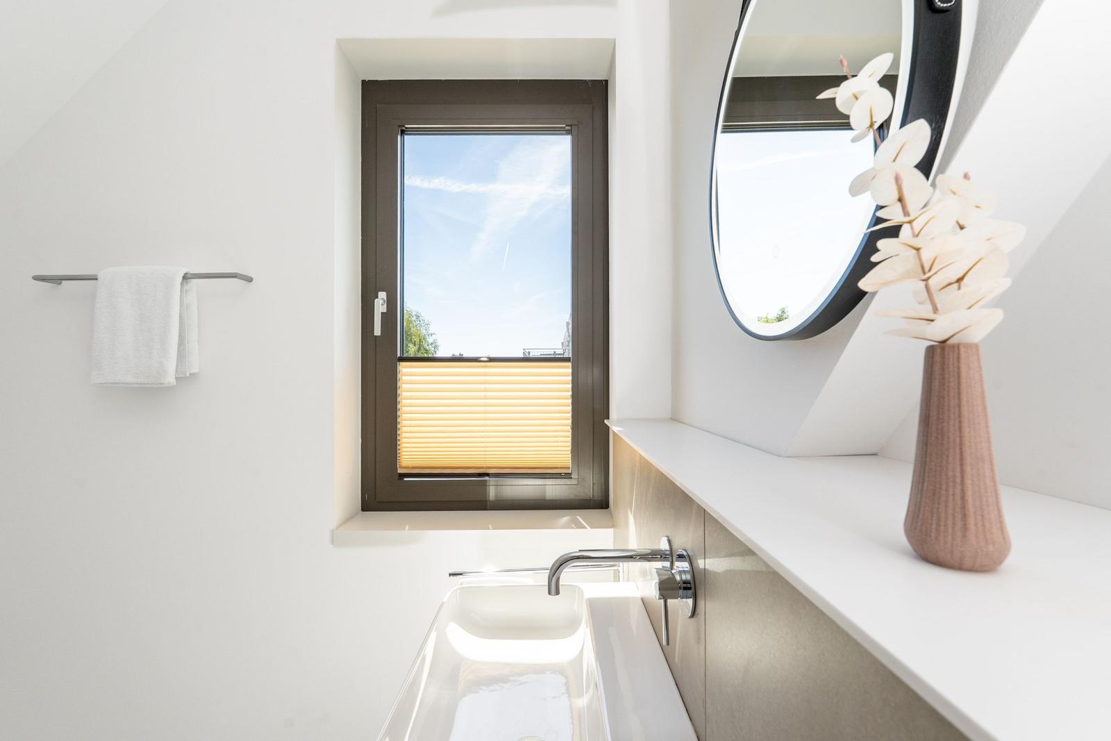 Badezimmer mit Waschbecken, Spiegel und Fenster mit Jalousie.