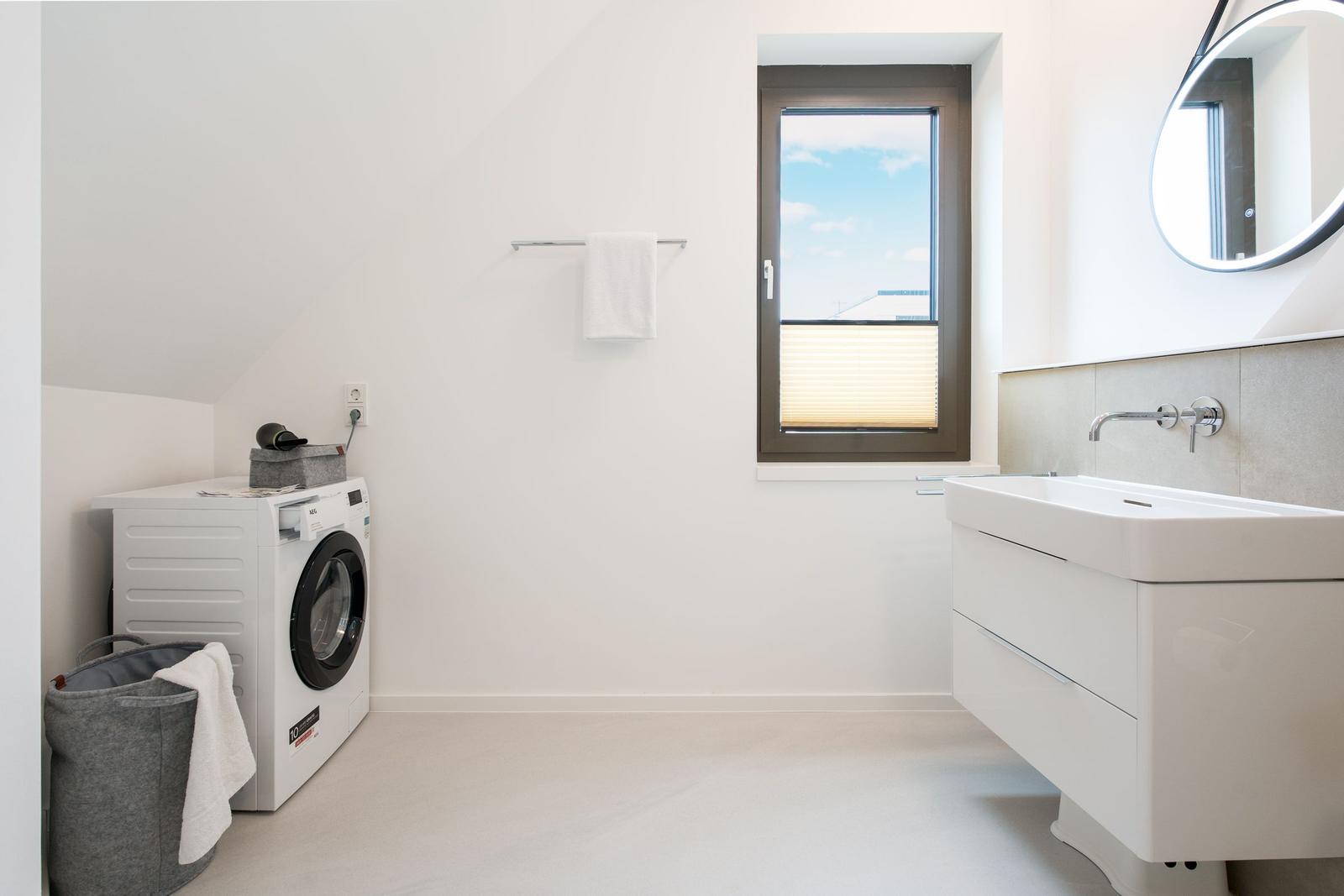 Badezimmer mit Waschmaschine, Waschtisch und Fenster.