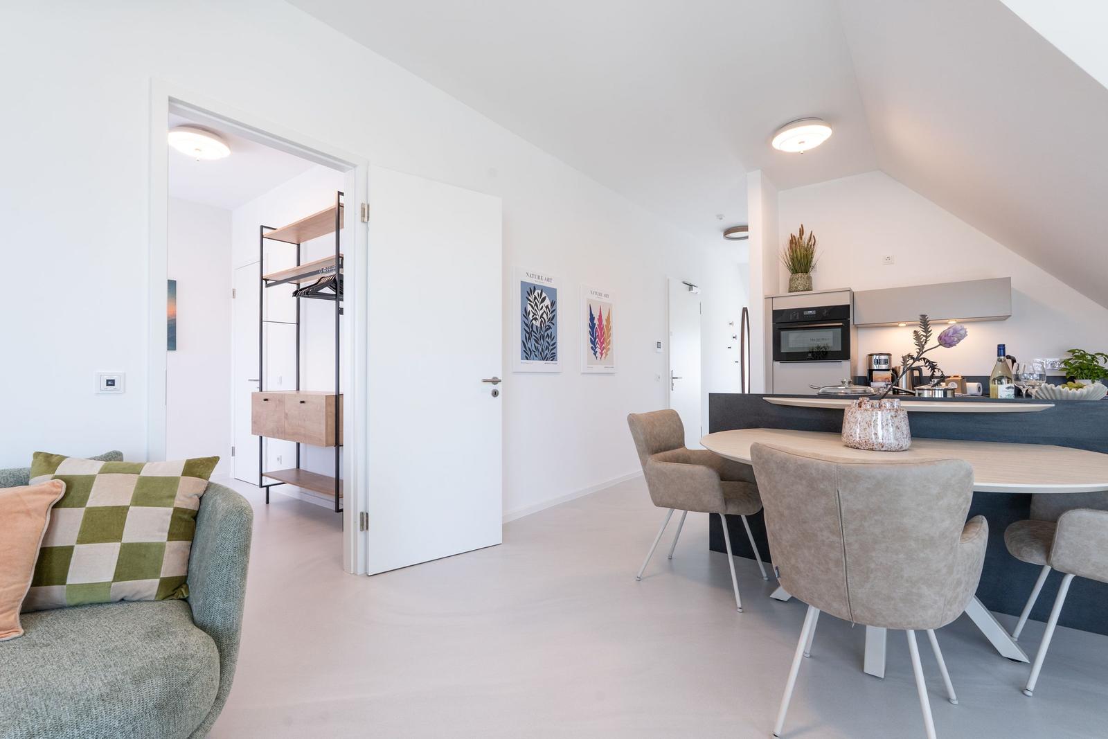 Wohn- und Essbereich mit Küchenzeile und Schlafzimmer im Hintergrund.
